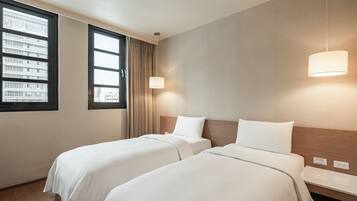 Een hotelkamer met twee bedden, een raam met gordijnen, een muurlamp en een houten hoofdeinde.
