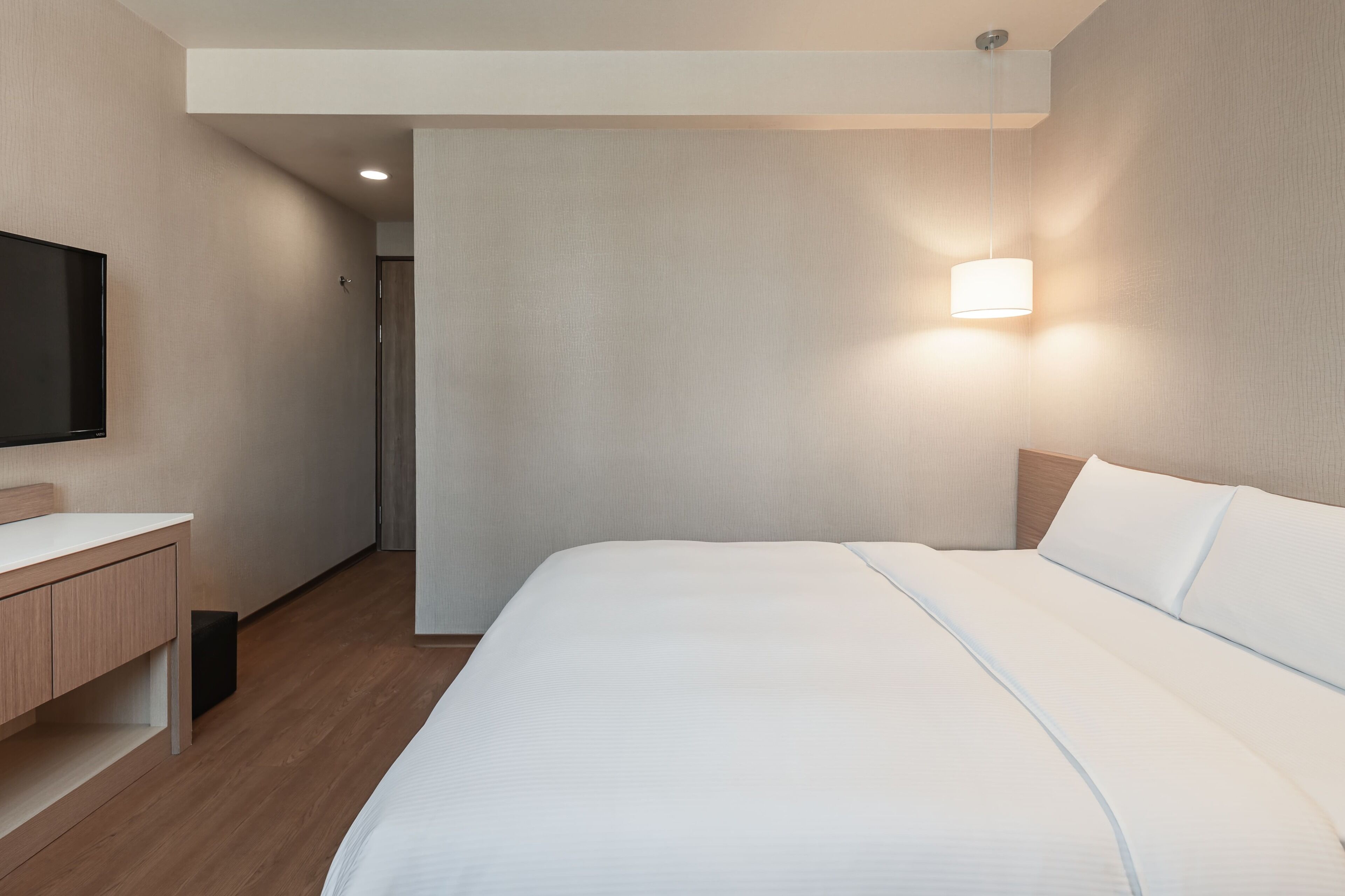 Una habitación de hotel moderna con una cama grande, una mesita de noche, un televisor de pantalla plana y una lámpara de pared.