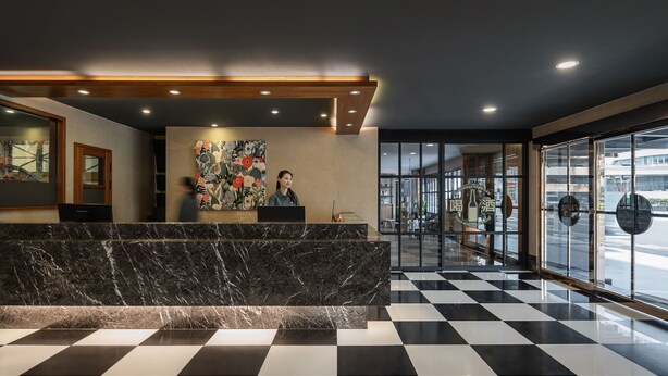 Een hotel receptie met een marmeren balie, een receptionist en een groot abstract schilderij aan de muur.