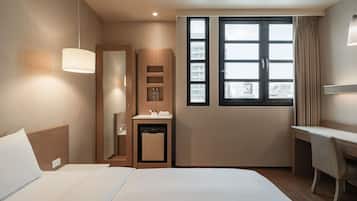Quarto de hotel com cama, escrivaninha, toucador e uma grande janela com vista para a cidade.