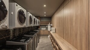 Een wasserette met meerdere wasmachines en drogers, houten kastjes en een wasbak.