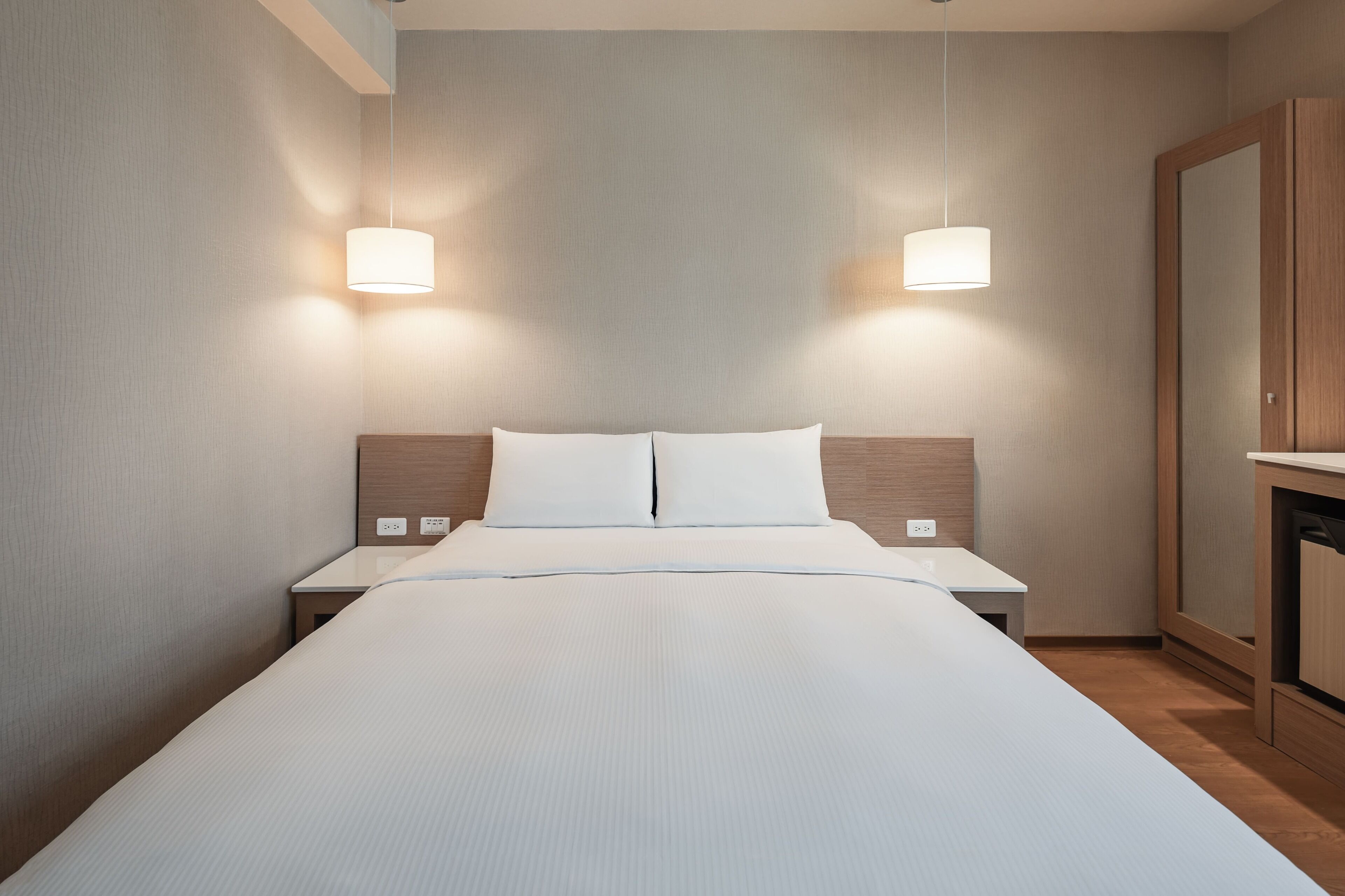 A modern hotel room with a large bed, bedside tables, and a wooden wardrobe.