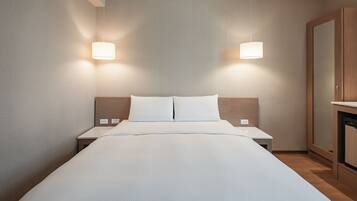 A modern hotel room with a large bed, bedside tables, and a wooden wardrobe.