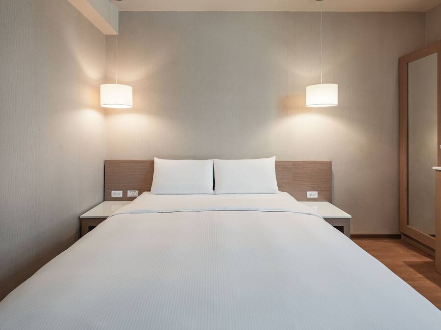 A modern hotel room with a large bed, bedside tables, and a wooden wardrobe.