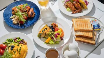 A table with various dishes including grilled chicken, a salad, a quiche, toast, and a cup of coffee.