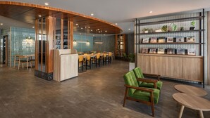Een moderne receptie met een gebogen houten receptiebalie, een groene bekleden fauteuil en een wandmontage van ingelijste objecten.