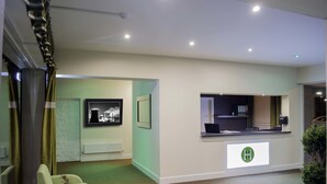 A hotel reception area with a reception desk, a framed picture on the wall, a radiator, and a green sofa with a plant. - Helix Hotel (Grangemouth)
