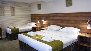 A hotel room with two beds, a wooden headboard, and a green accent on the bed. There are two nightstands with lamps and a wall-mounted outlet. - Helix Hotel (Grangemouth)