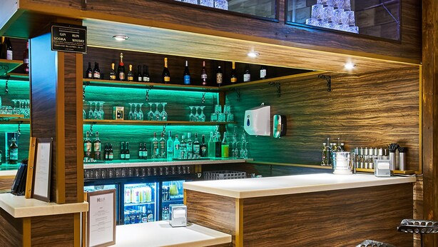 A bar area with wooden paneling, a refrigerated display case, and bar stools. - Helix Hotel (Grangemouth)