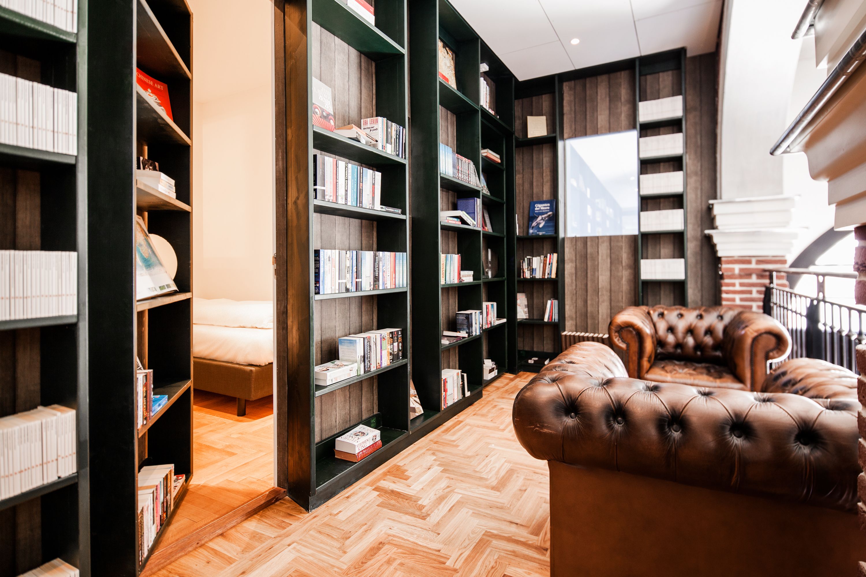 A library with bookshelves, a leather armchair, and a bed.
