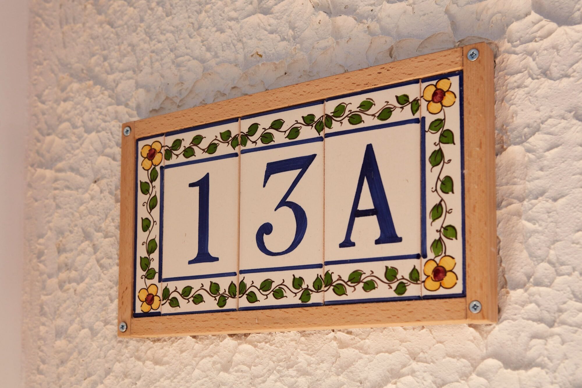 Una placa de número de casa con el número 13A, rodeada de motivos florales decorativos.