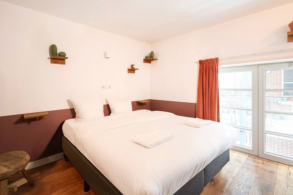 A hotel room with a bed, a bench, and a window with curtains.