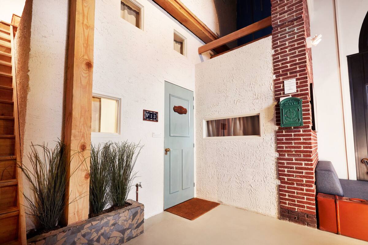 A building with a blue door, a stone planter with plants, and a brick wall with a green plaque.