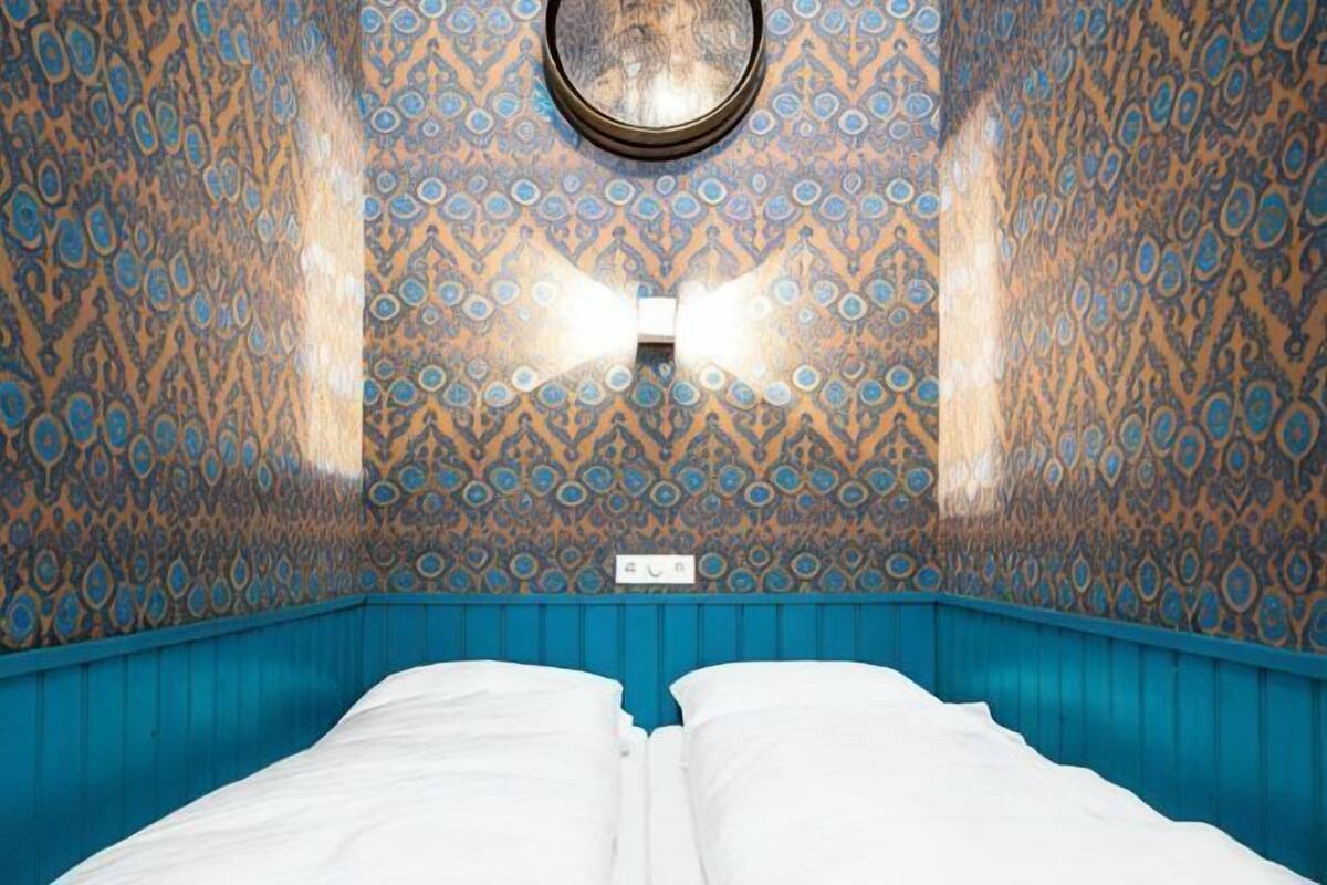 A room with a patterned wall, a bed with white bedding, and a circular light fixture on the ceiling.