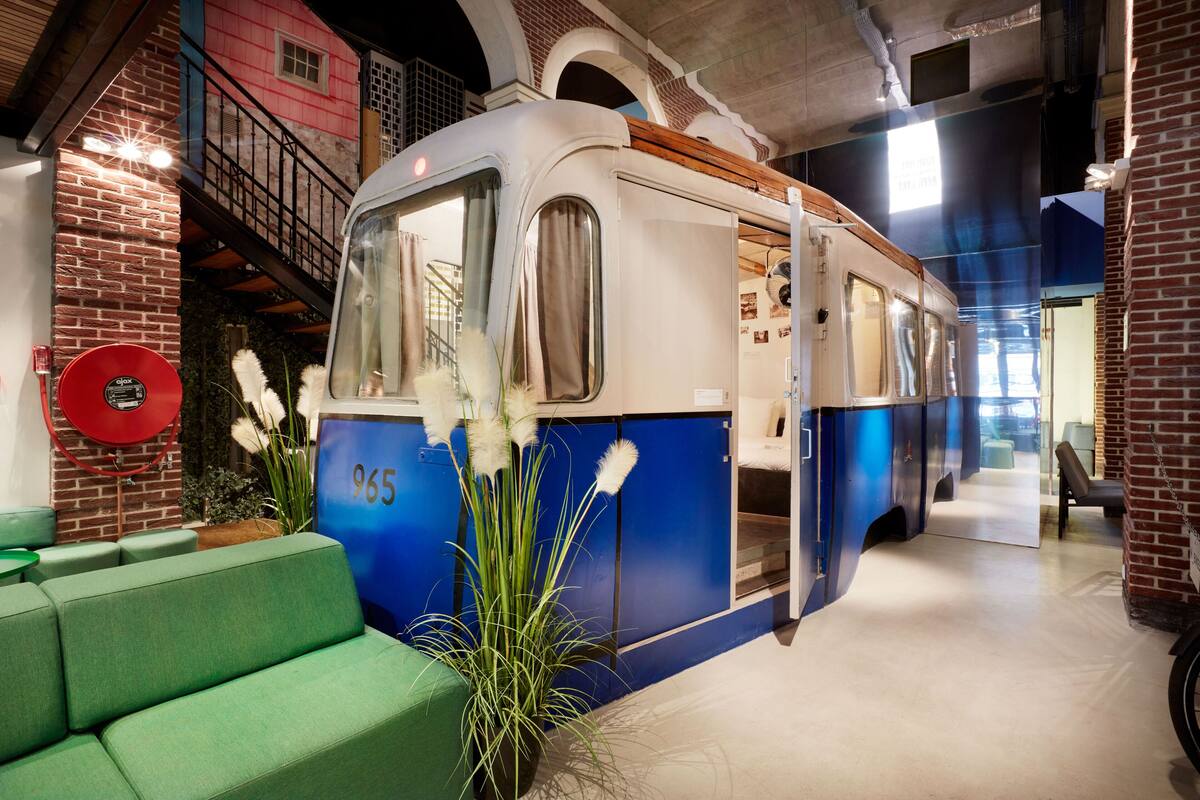 A vintage train car suspended in a lobby with green seating and a brick wall.