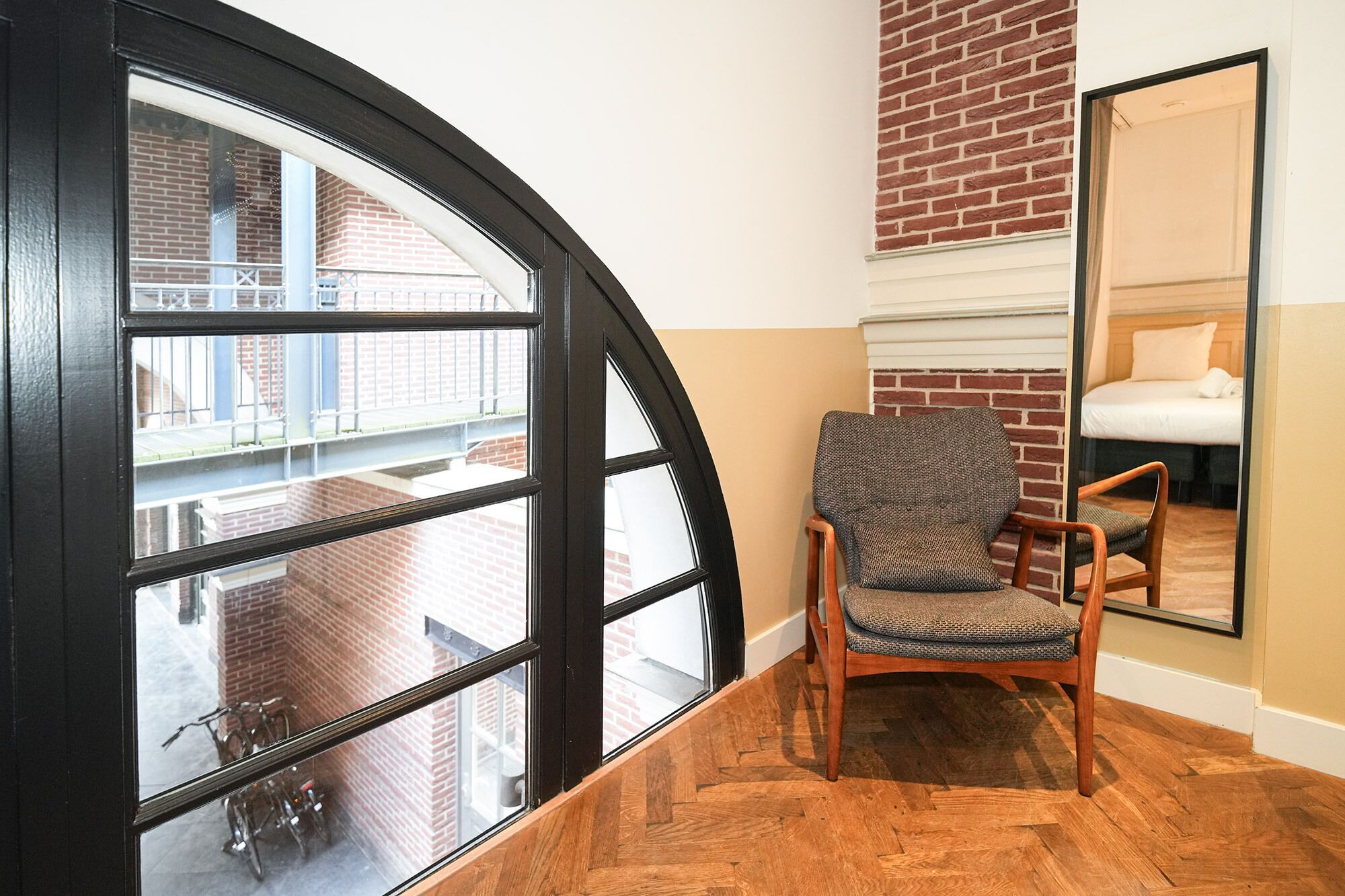 Hotellihuone, jossa on kaareva ikkuna, tuoli, sänky ja peili.