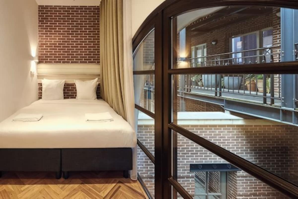 Una camera d'albergo con un letto, un muro in mattoni, una finestra e vista all'esterno.