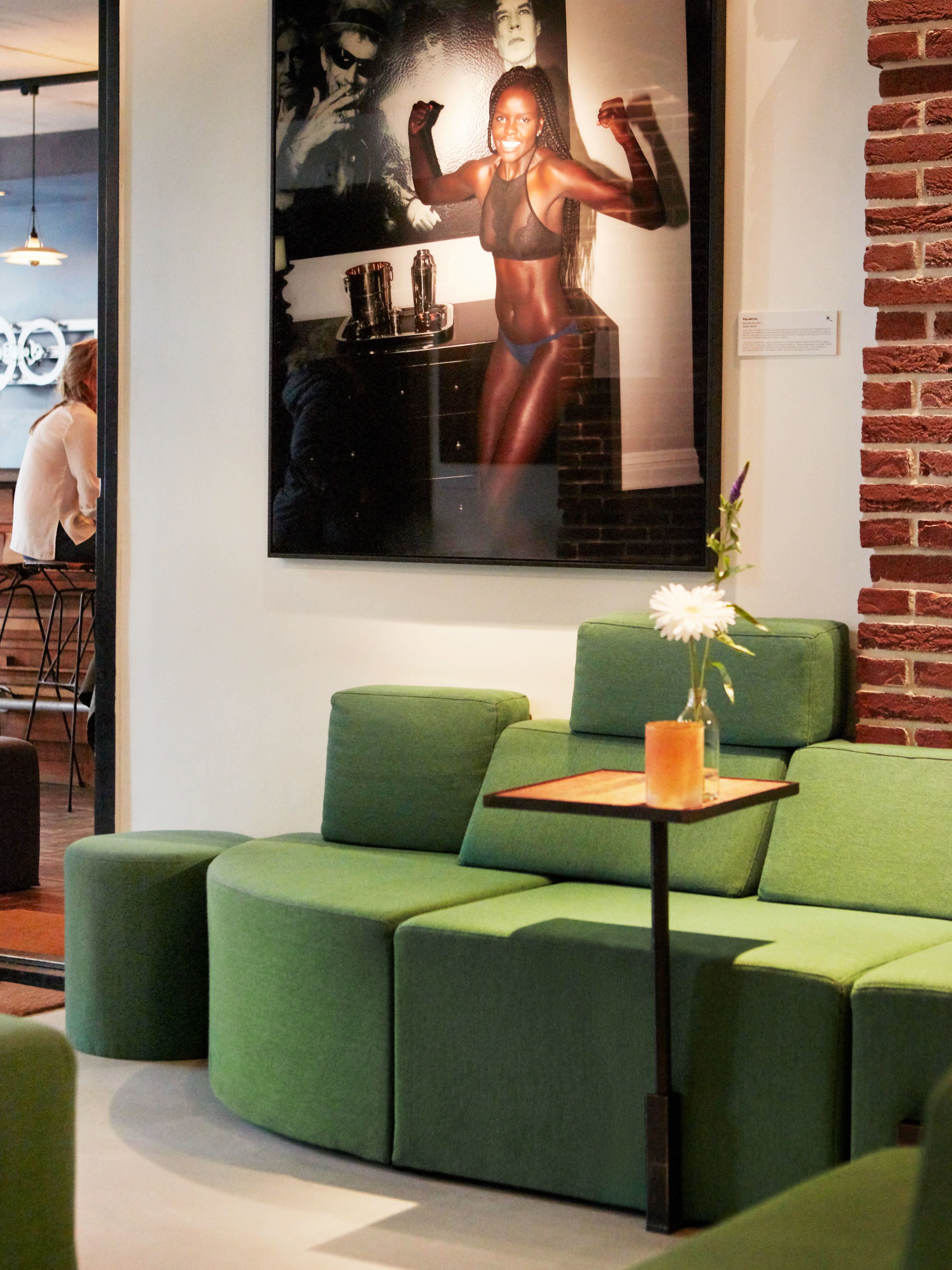 Een modern interieur met een groene modulaire bank, een klein tafeltje met een vaas en een ingelijste foto aan de muur.