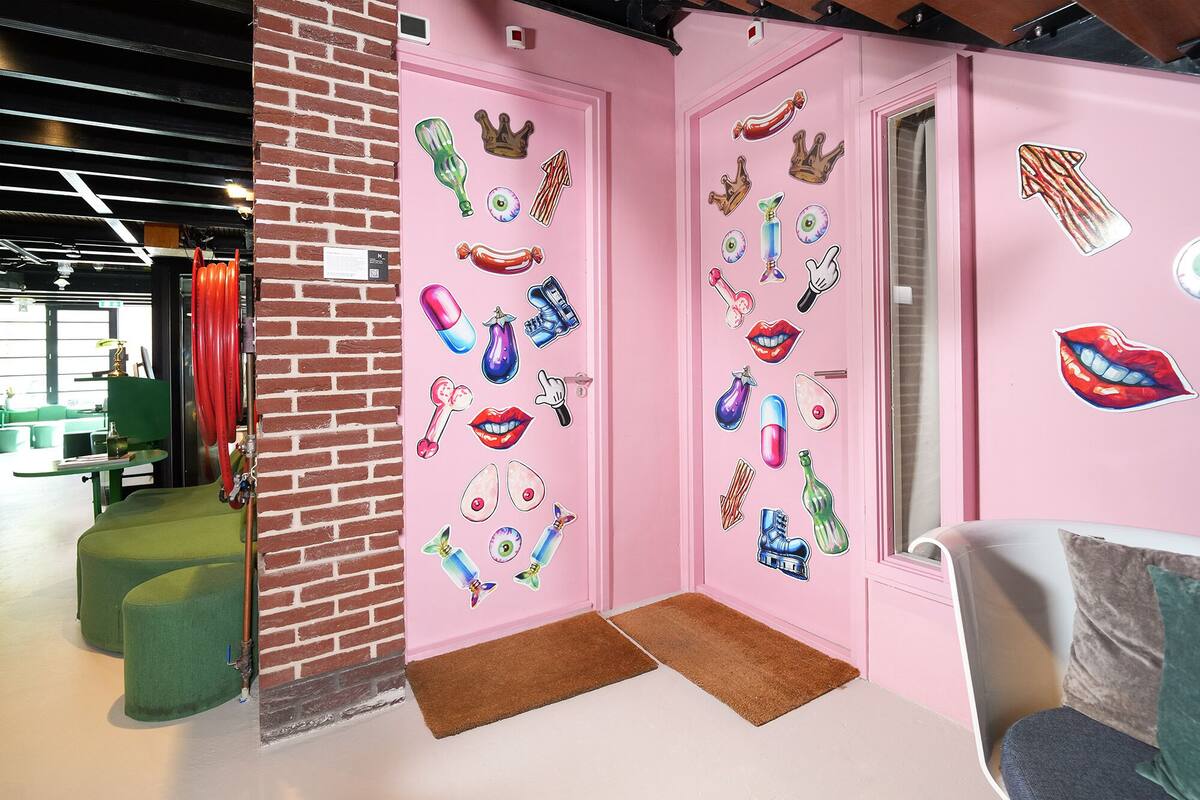 A pink wall with various stickers, a green cushioned bench, and a door with a doormat.