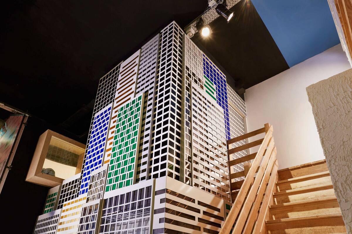 A model of a multi-story building with a grid-like facade, wooden staircases, and a visible window on the left side.