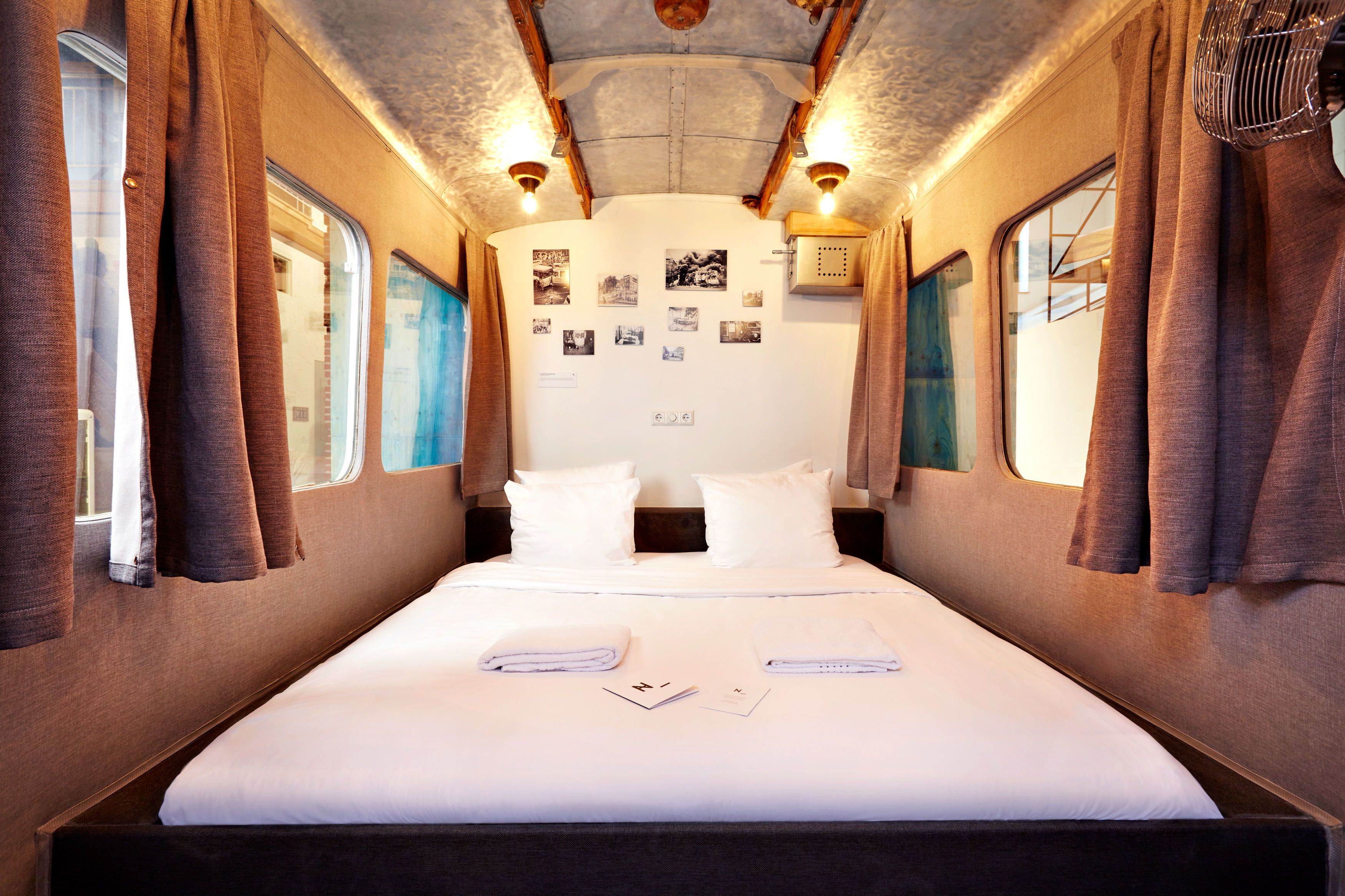A train bedroom with a single bed, curtains, and wall-mounted lights.