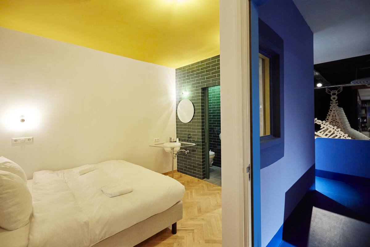 A bedroom with a bed, a bedside table, and a bathroom visible through an open door.