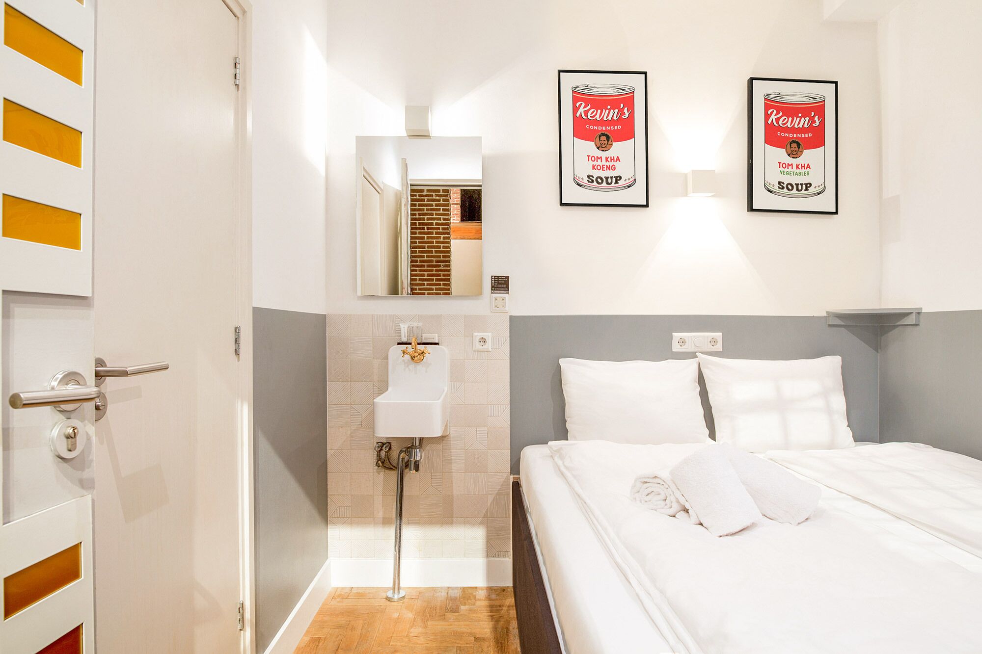 A hotel room with a bed, a bathroom with a sink and shower, and two framed pictures on the wall.