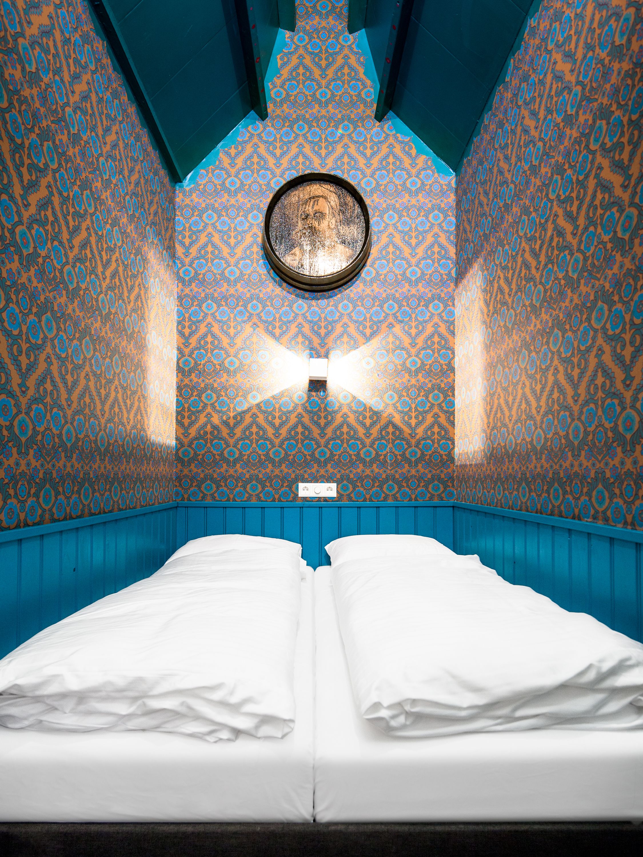 A room with a bed, patterned walls, and a circular window.