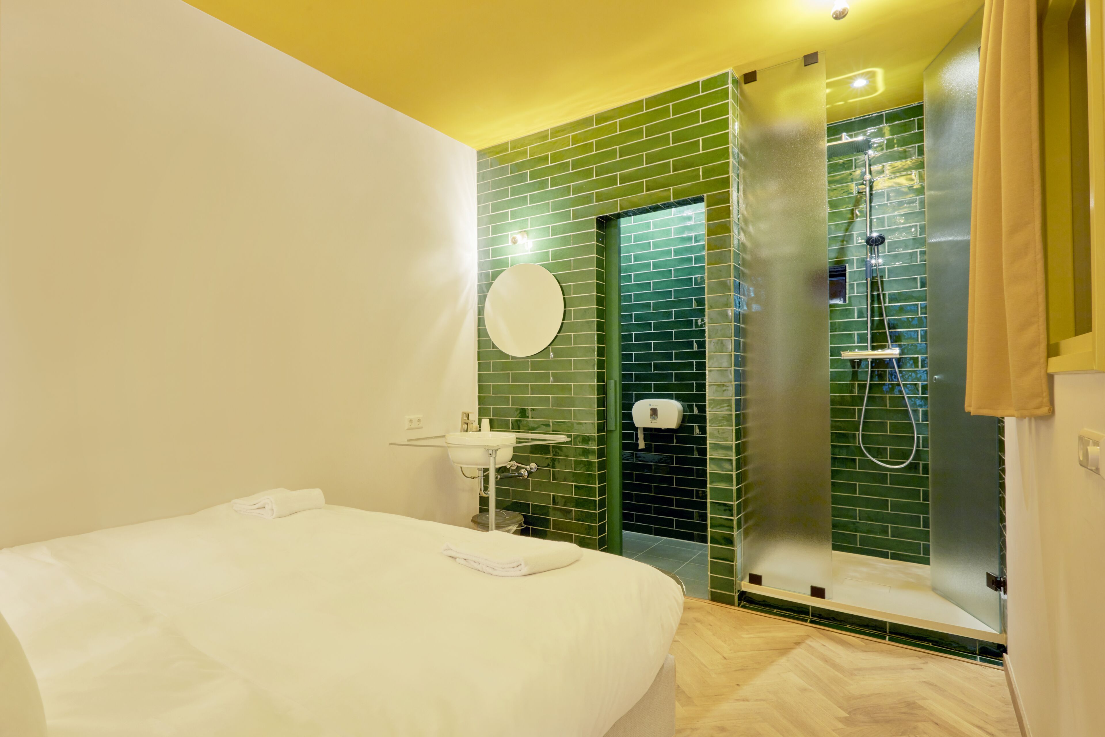 A hotel room with a bed, a sink, and a shower area.