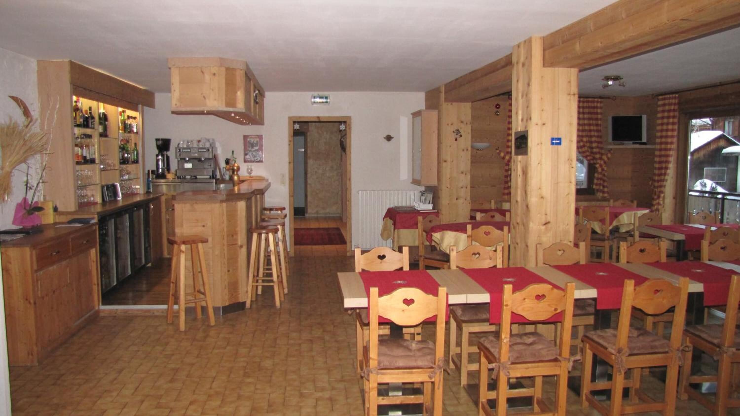 Een rustiek houten interieur met een bar, houten tafels en stoelen, en een zichtbare keukenhoek.