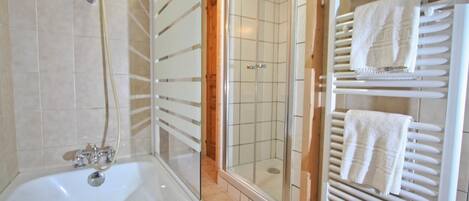 Een badkamer met een bad, een douche met glazen wanden en een handdoekrek met handdoeken.