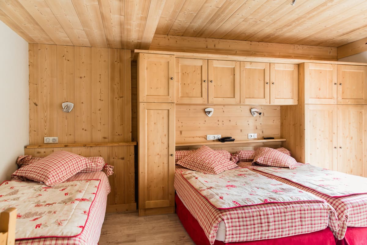 A wooden room with two beds, each with red and white bedding, and wooden cabinets above.