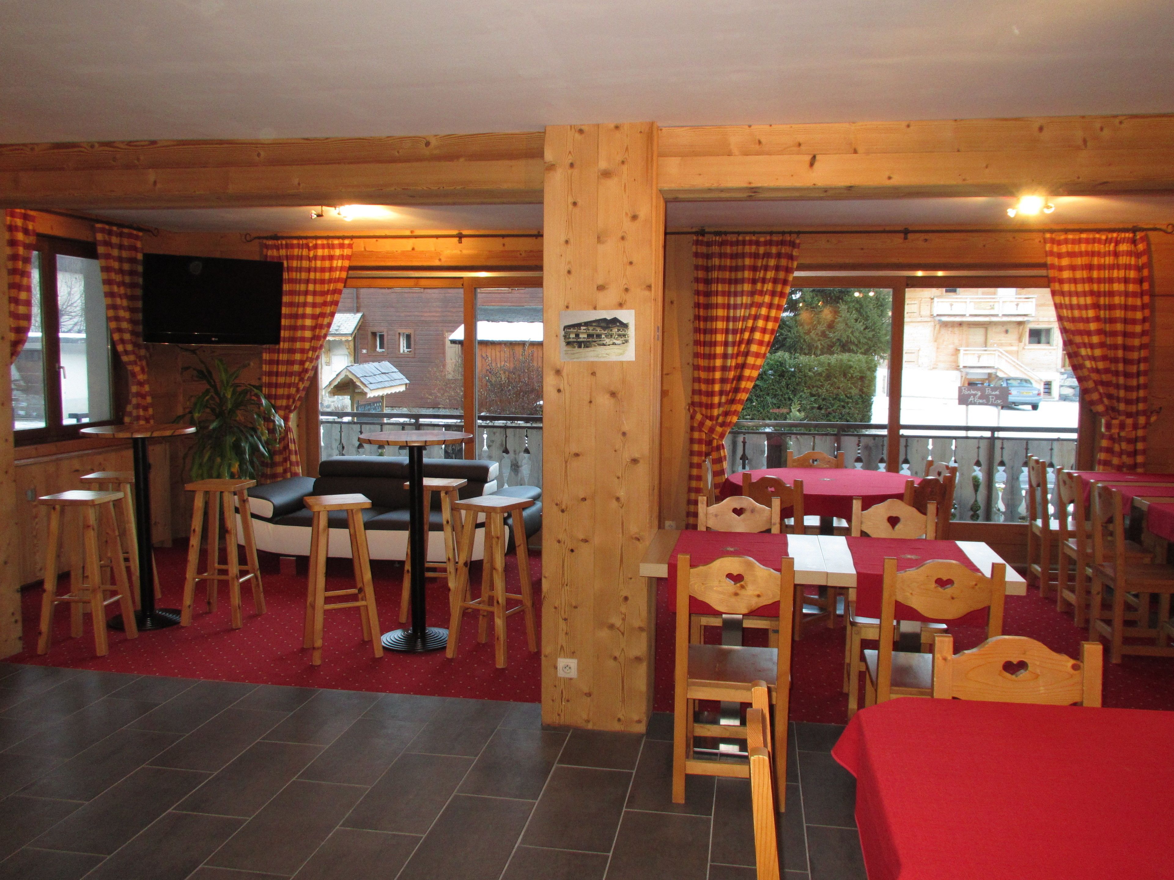 A cozy restaurant with wooden interiors, a terrace with tables and chairs, and a view of the street.