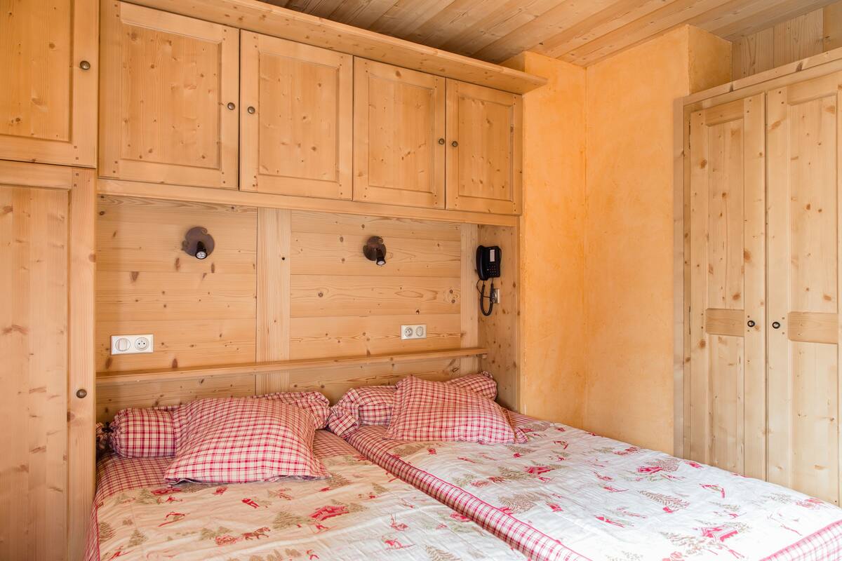 A wooden cabin bedroom with a bed, checkered bedding, a telephone, and a wooden wardrobe.