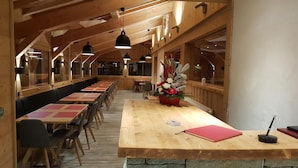 A restaurant with a long wooden table and benches, stone accents, and a flower arrangement. - Hôtel Alpen Roc (Morzine)