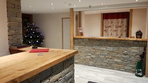 A reception area with a wooden counter, stone wall, and a Christmas tree. - Hôtel Alpen Roc (Morzine)