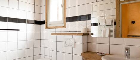Een badkamer met witte betegelde wanden, een houten wastafelmeubel, een wastafel, een spiegel en een raam.
