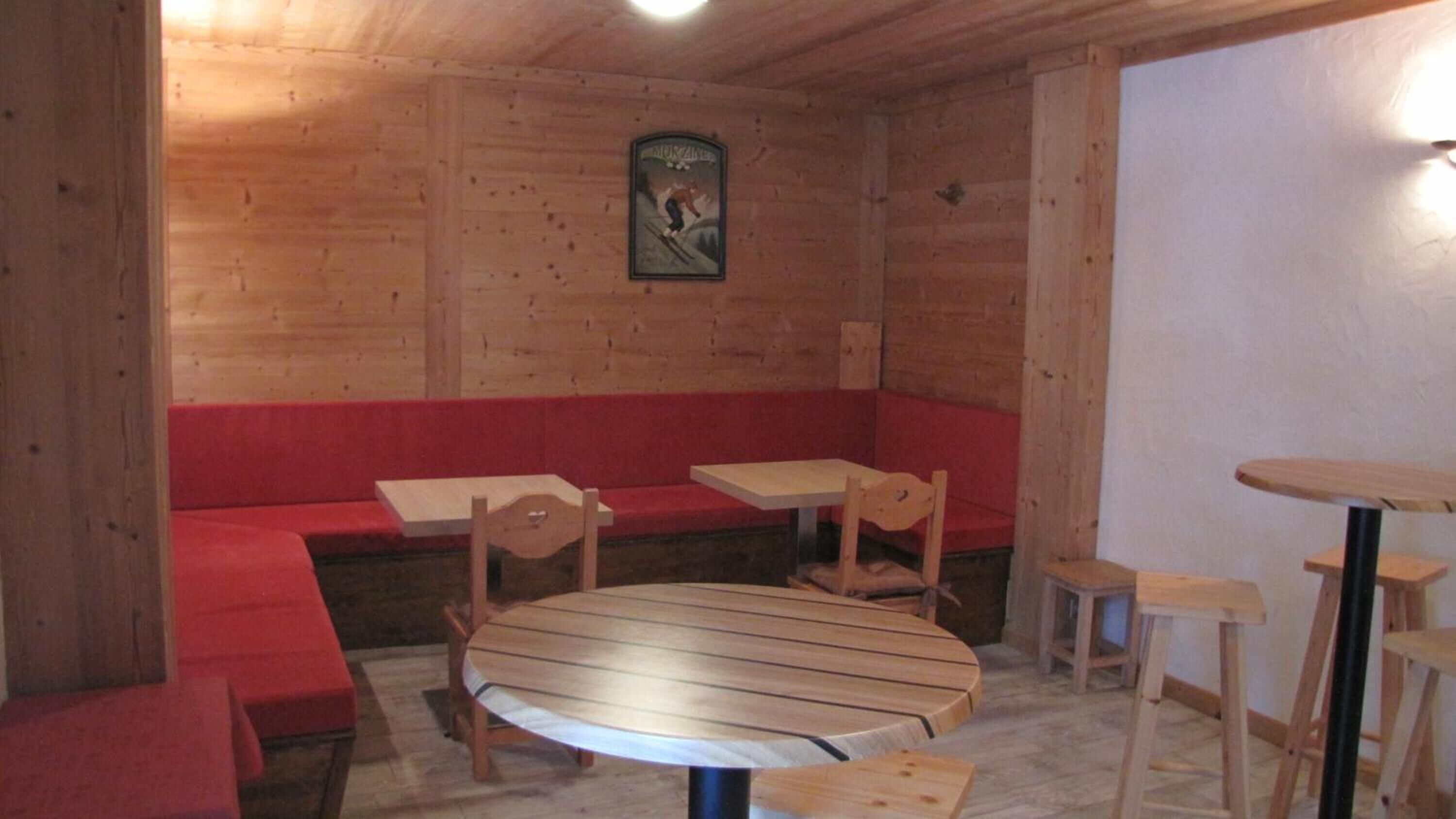 Un intérieur en bois avec une table ronde, des bancs et un petit tableau accroché au mur.
