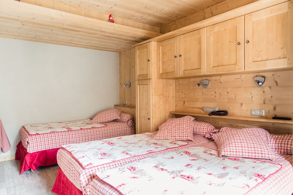 A bedroom with two beds, wooden cabinets, and a small shelf with items.