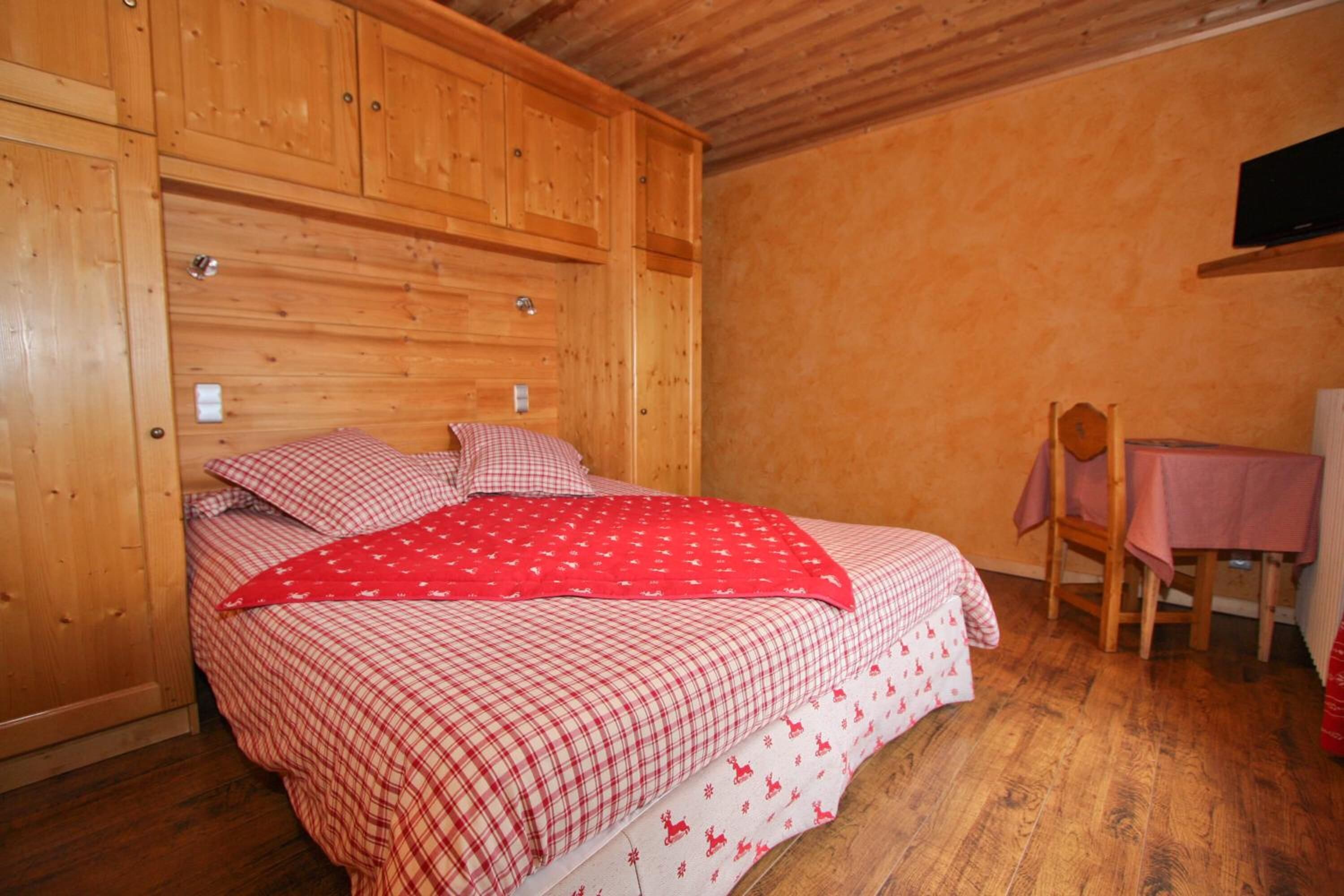 A wooden bedroom with a bed, a chair, and a table.