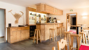 A bar area with wooden stools, a counter with bottles, and a wooden cabinet with drawers. - Hôtel Alpen Roc (Morzine)