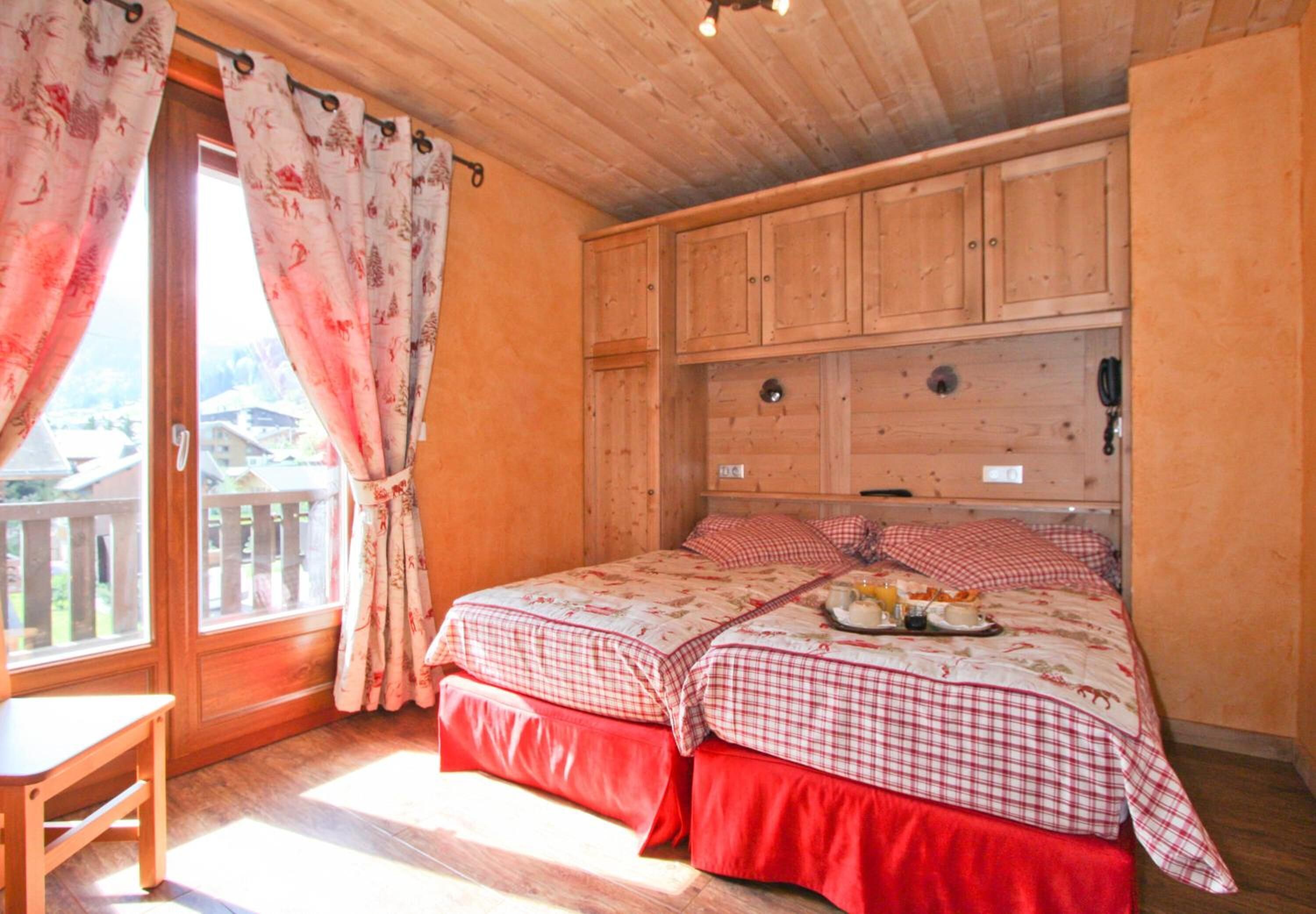 Une chambre dans une cabane en bois, avec un lit, une tête de lit en bois et une fenêtre avec des rideaux.