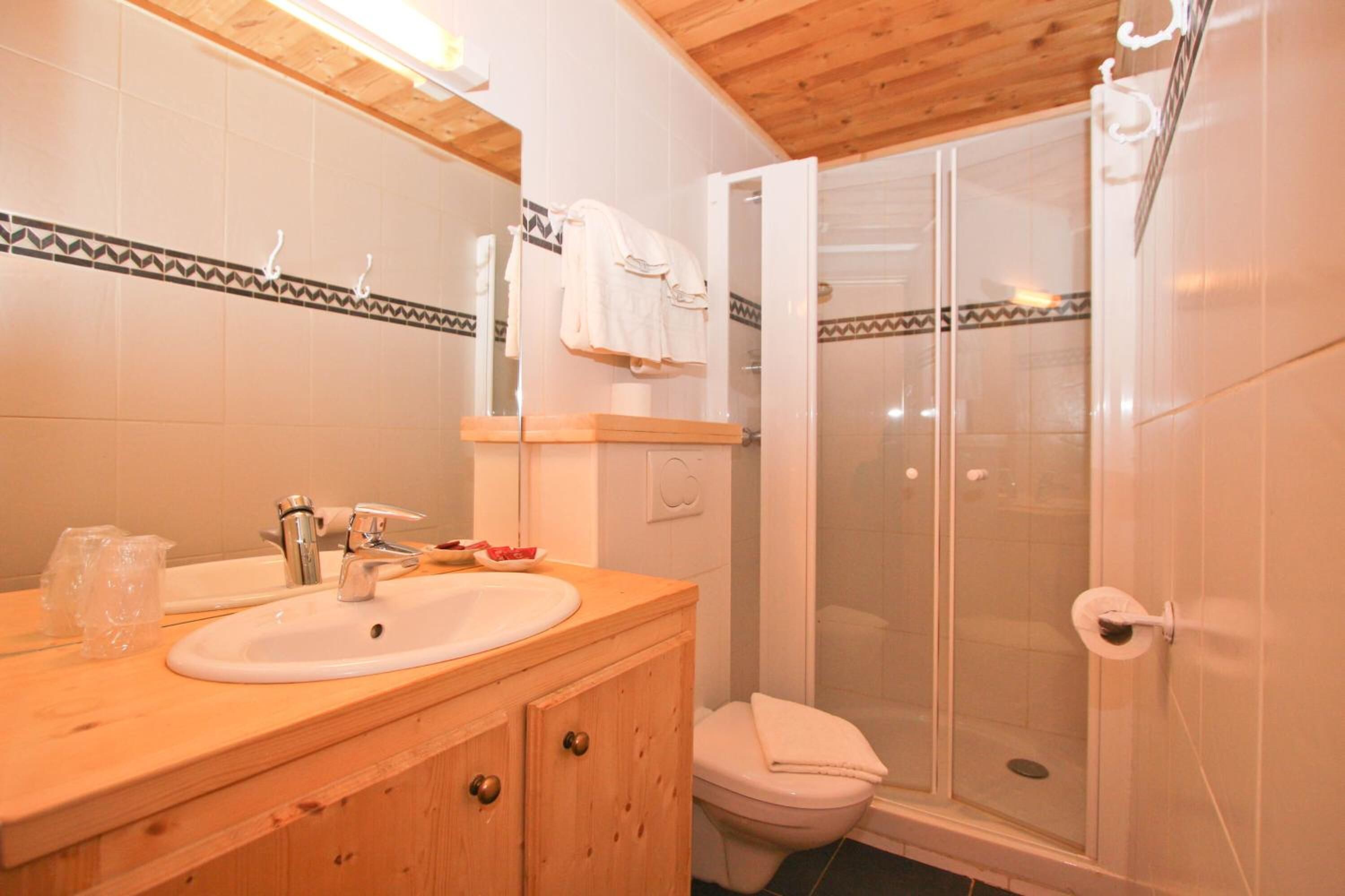 Une salle de bain avec un meuble-lavabo en bois, un évier, des toilettes et une douche à parois de verre.