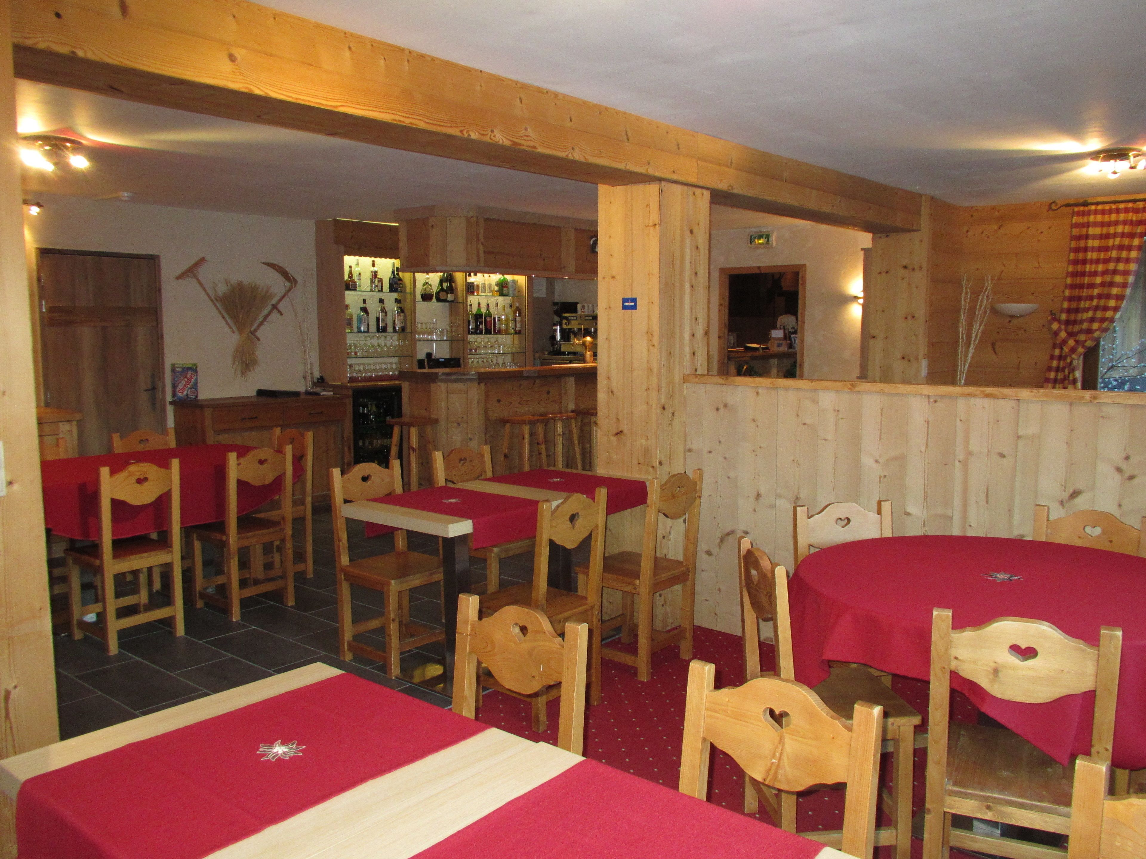 A restaurant with wooden interiors, tables with red tablecloths, and a bar area.