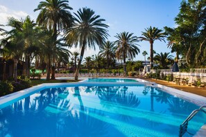 A swimming pool surrounded by palm trees and lounge chairs, with a clear sky above. - HL Miraflor Suites (San Bartolomé de Tirajana)
