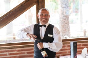 A person in a white shirt and black vest opening a bottle of wine. - HL Miraflor Suites (San Bartolomé de Tirajana)