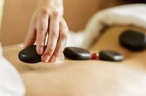 En hand som utövar tryck på en massage­sten på en persons rygg.