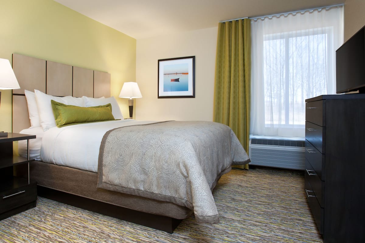 A hotel room with a bed, two bedside lamps, a flat-screen TV, a dresser, and a framed picture on the wall.