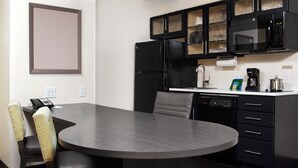 A modern kitchen with a built-in microwave, refrigerator, and dishwasher. There is a dining table with chairs and a telephone on the counter.