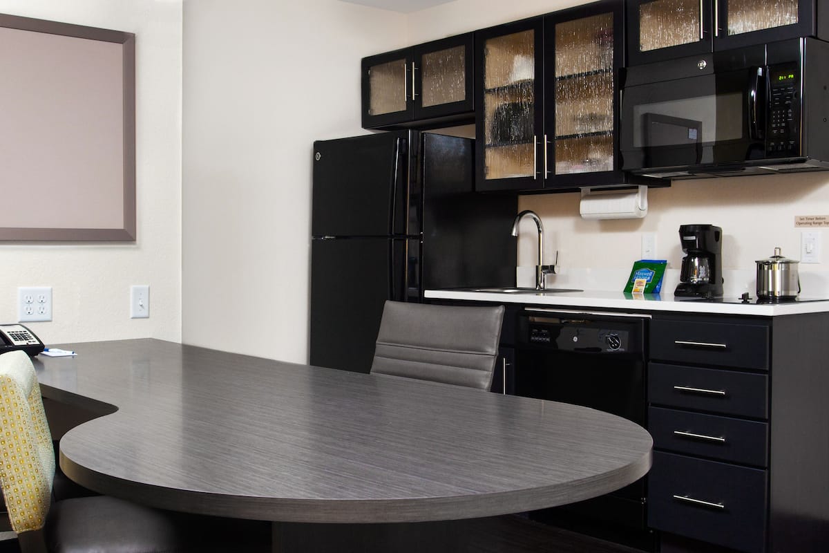 A modern kitchen with a built-in microwave, refrigerator, and dishwasher. There is a dining table with chairs and a telephone on the counter.